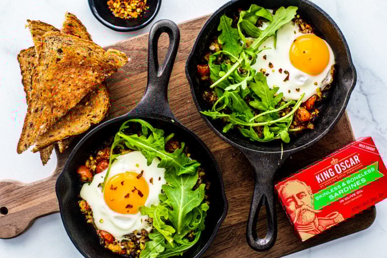 Two miniature skillets filled with Fisherman's Eggs and topped with arugula.