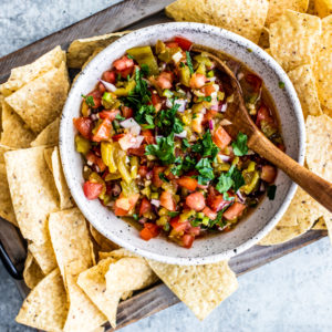 Bowl of roasted hatch chile salsa on a platter of tortilla chips.