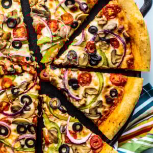 Sliced up veggie deluxe pizza on a cast iron pan.