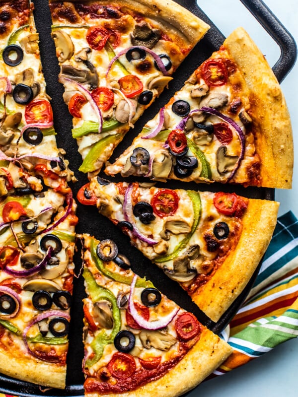 Sliced up veggie deluxe pizza on a cast iron pan.