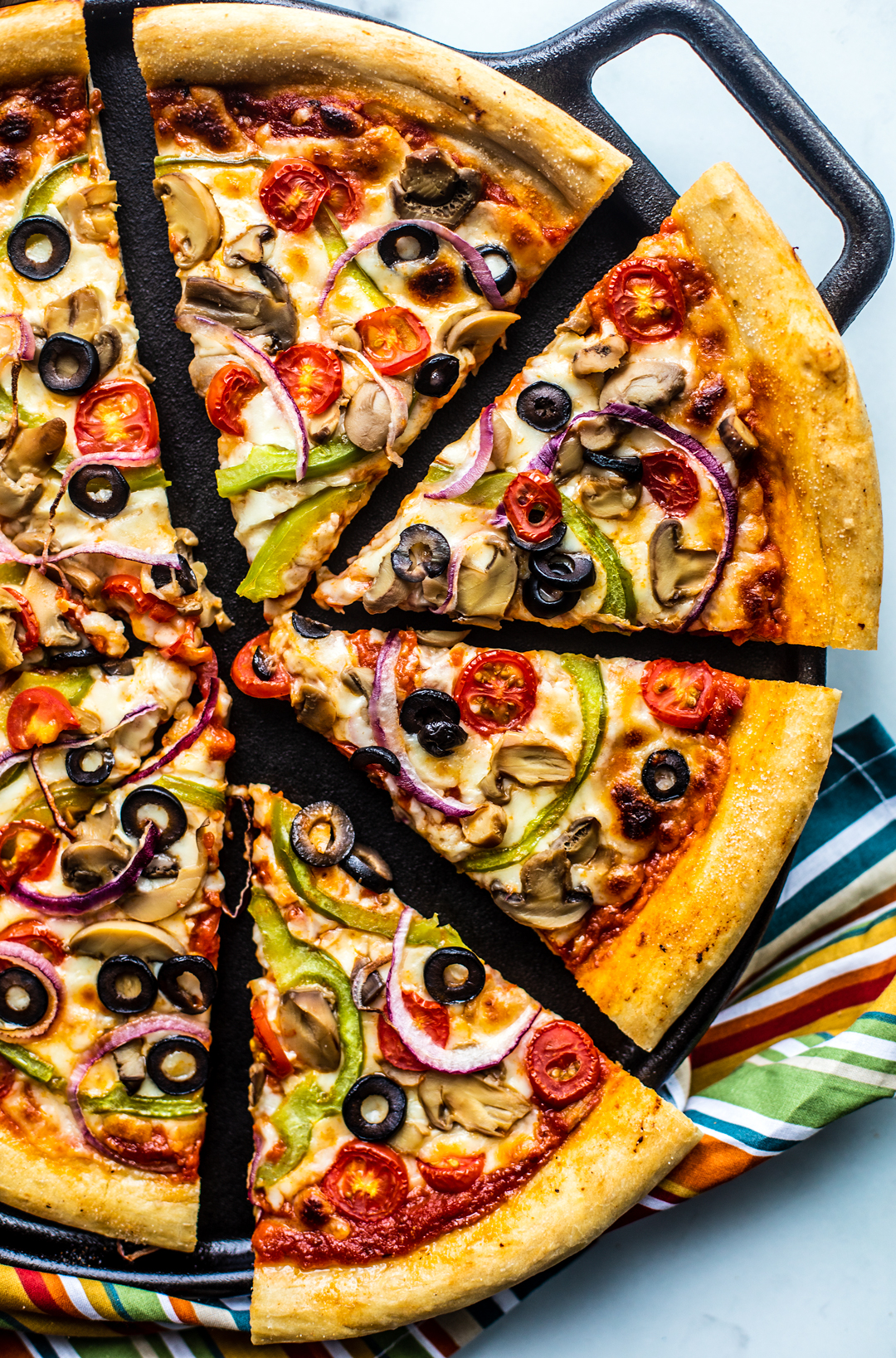 Sliced up veggie deluxe pizza on a cast iron pan.