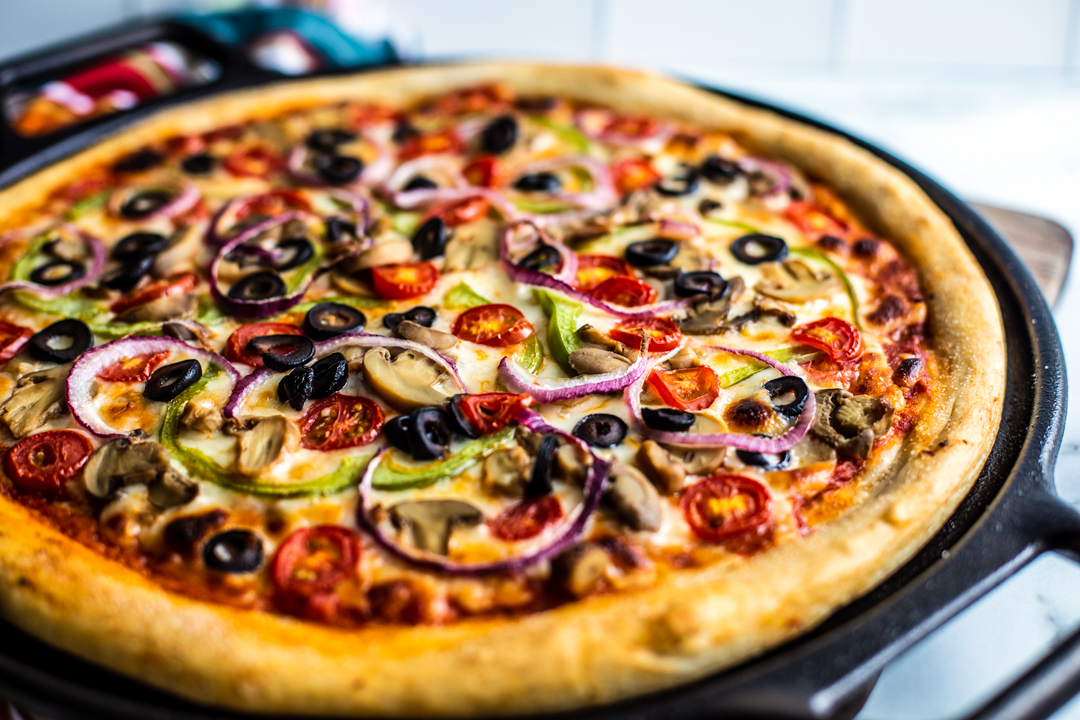 Side shot of veggie deluxe pizza, cooked, in pizza pan.