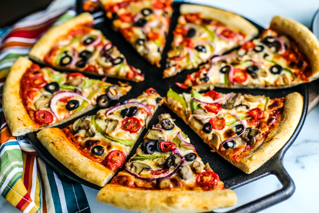 Sliced up veggie deluxe pizza on a cast iron pan.