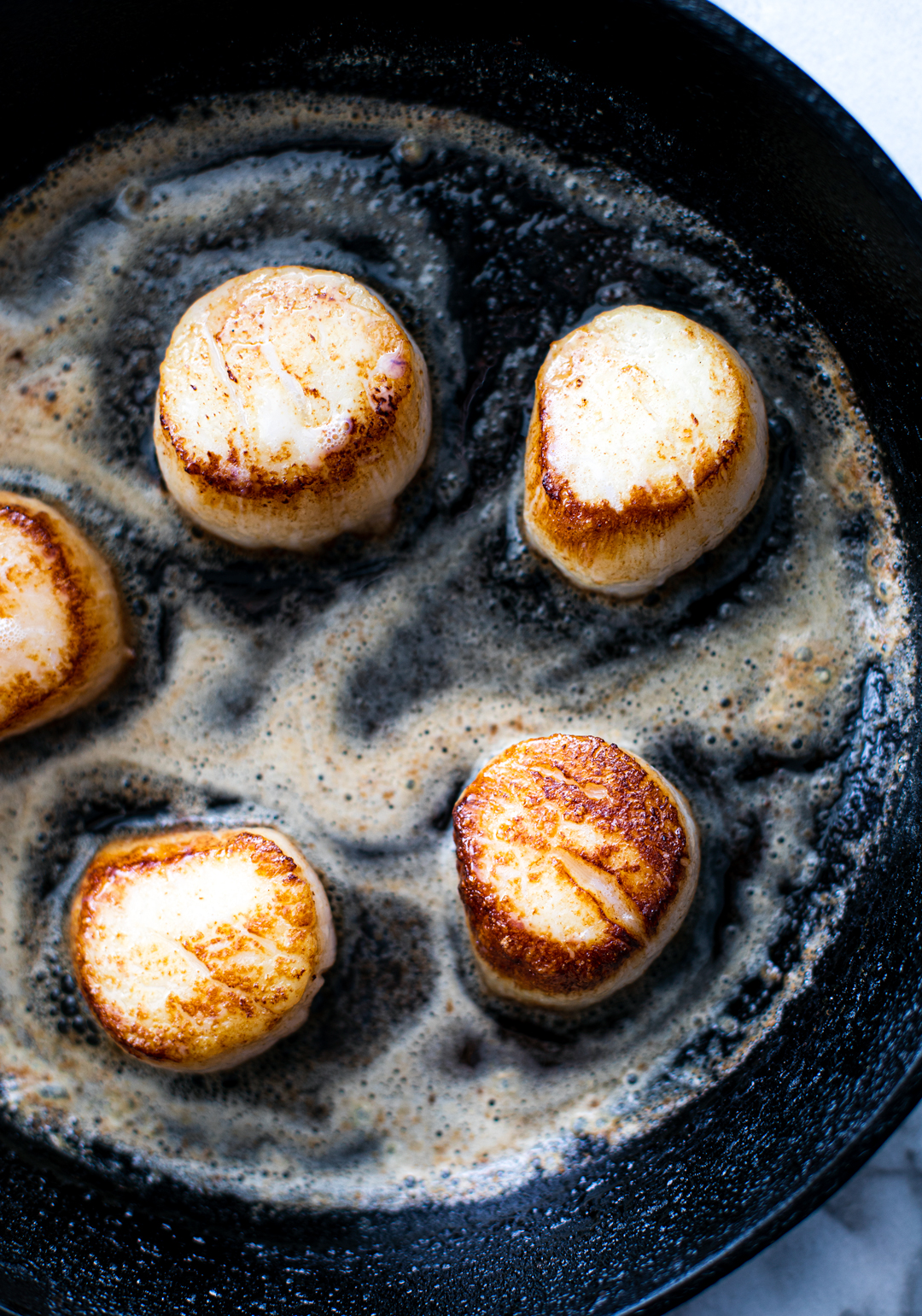Seared scallop in a pan full of melted butter.