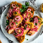 Serving plate full of crispy pork schnitzel topped with pickled onions and apples, and parsley.