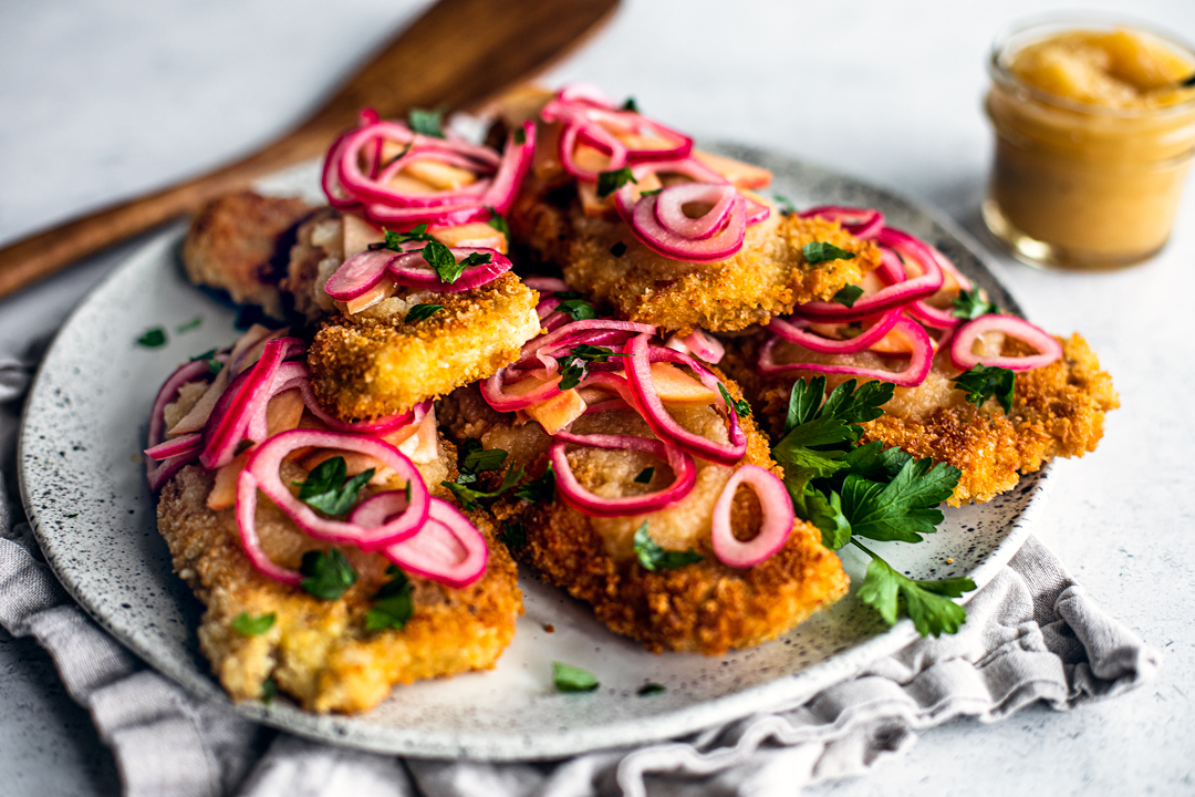 Serving plate topped with pork schnitzel and pickled onions and apples.