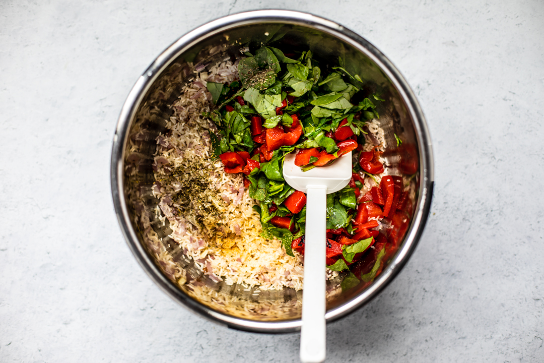 Overhead shot of rice, spices, spinach, and roasted red peppers in Instant Pot.