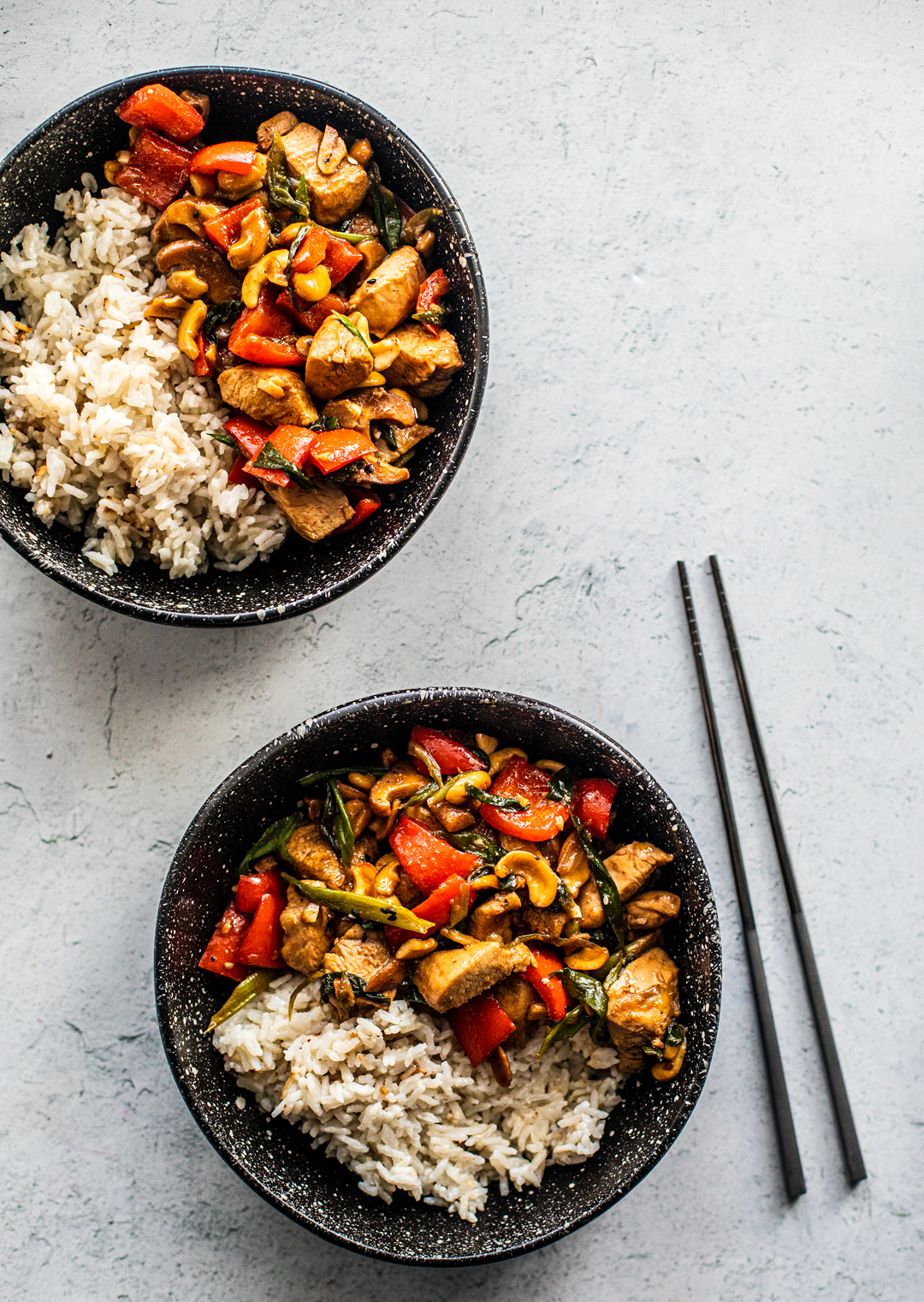 Two bowls of cashew chicken with rice and a set of chopsticks.