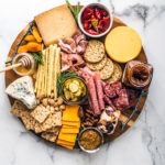 Overhead view of meat and cheese platter with nuts, fruits, jams, honey, etc.