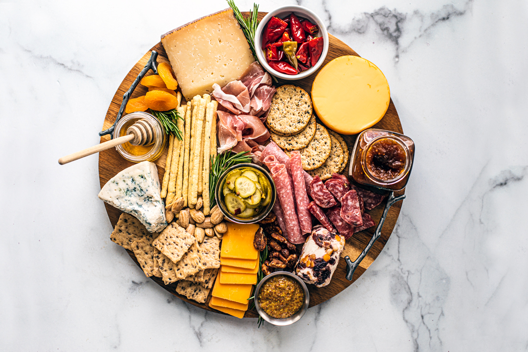 Overhead view of meat and cheese platter with nuts, fruits, jams, honey, etc.