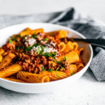 Side shot of bowl of rigatoni topped with turkey bolognese.