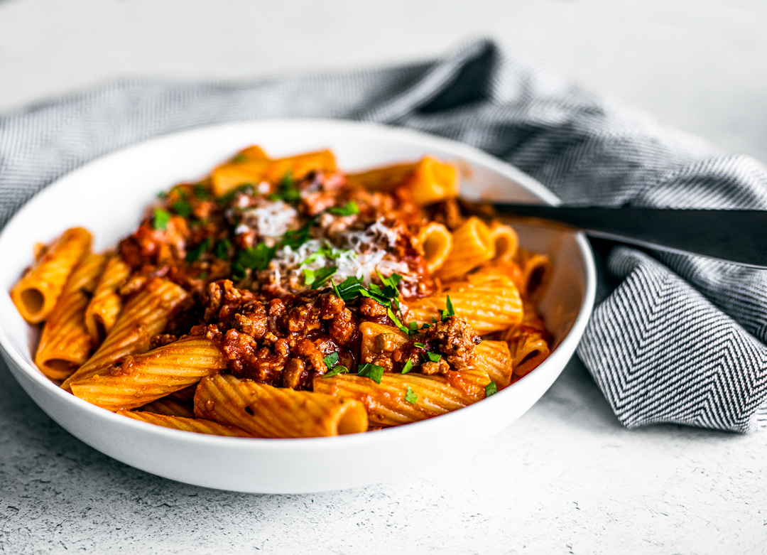 Side shot of bowl of rigatoni topped with turkey bolognese.