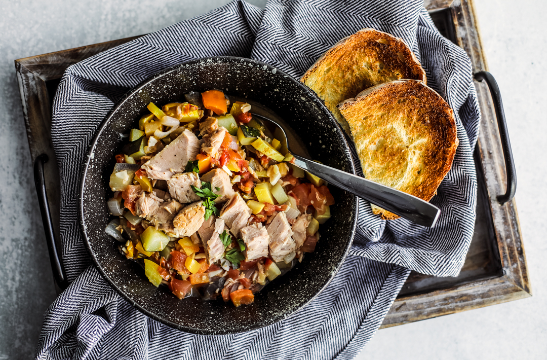 Overhead shot of bowl of ratatouille with tuna and crusty bread on a serving tray.
