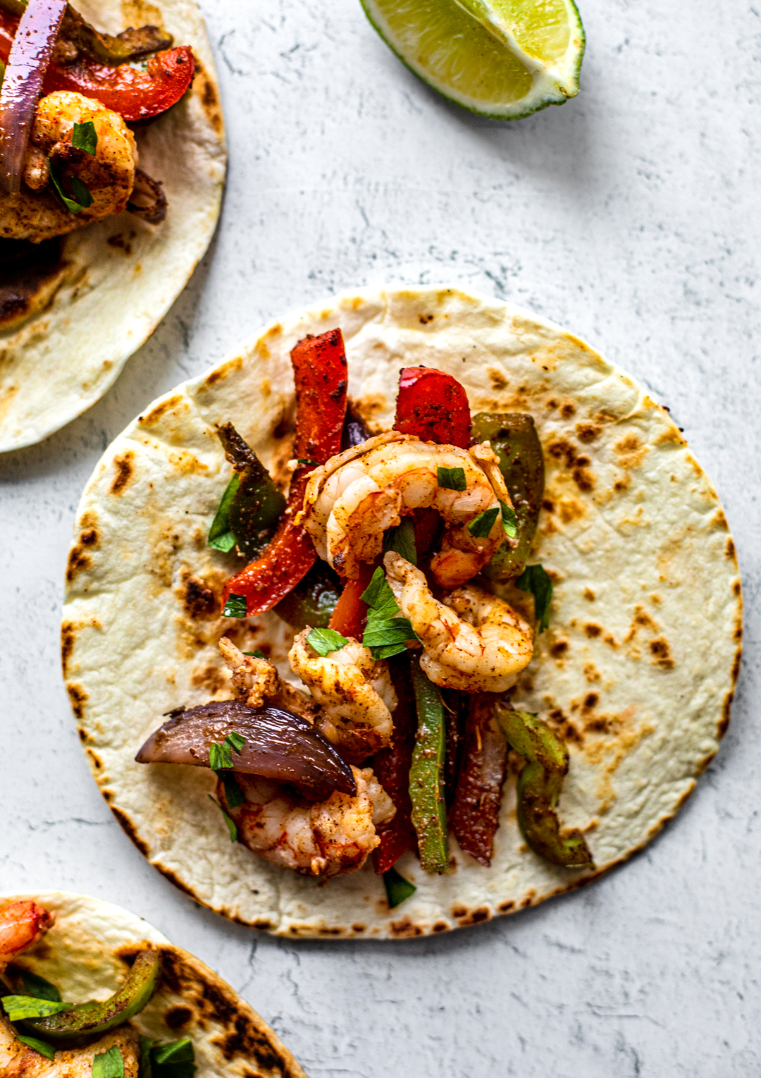 Overhead shot of flour tortillas topped with onions, peppers, and shrimp.
