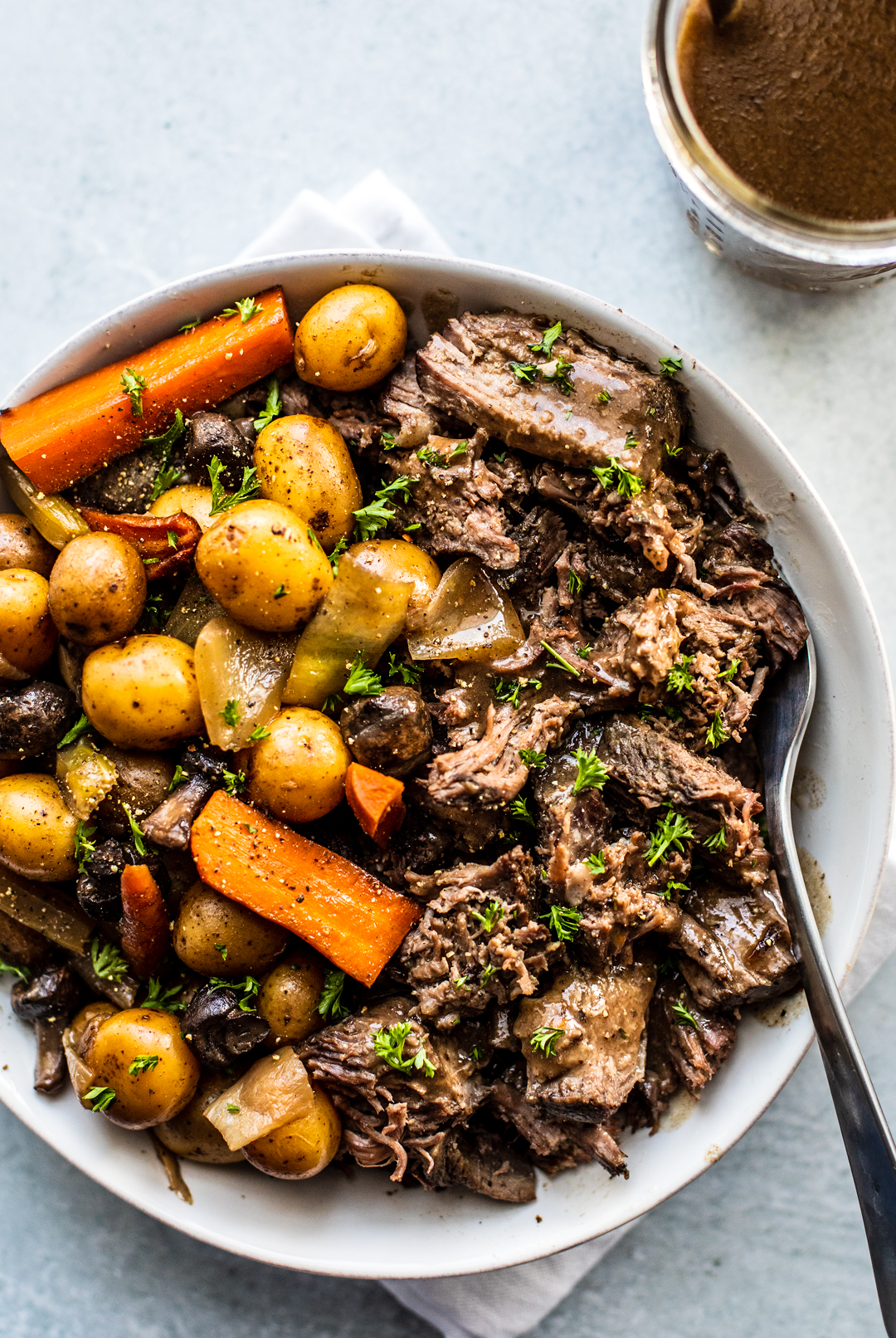 Overhead shot of shredded pot roast in serving dish with potatoes, carrots, and mushrooms.