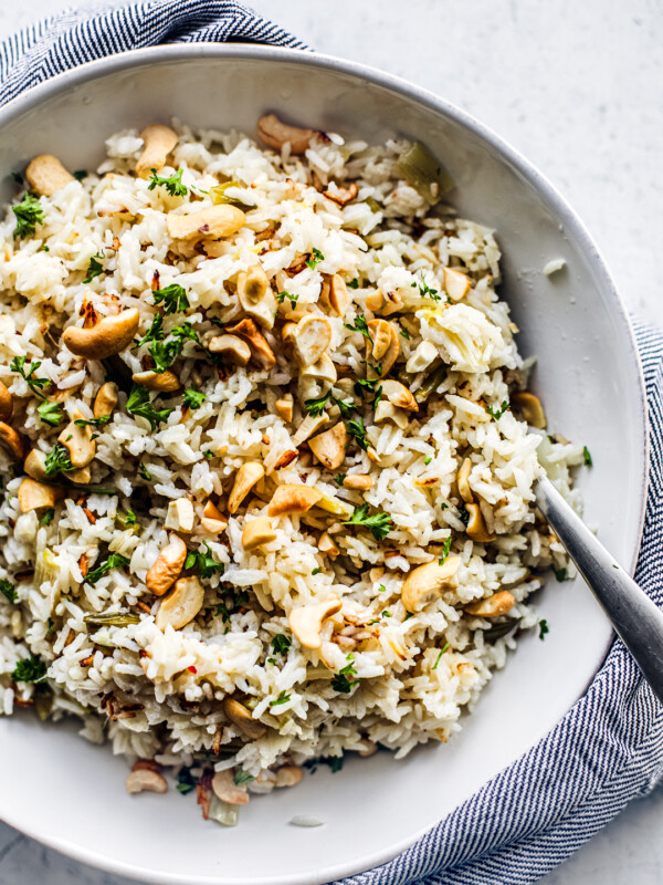 Close up of serving bowl full of coconut rice topped with cashews and a lime.
