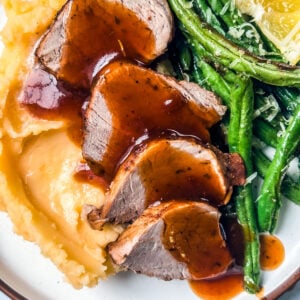 Pork medallions drizzled with sauce over mashed potatoes and green beans.