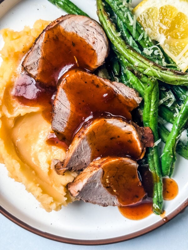 Pork medallions drizzled with sauce over mashed potatoes and green beans.