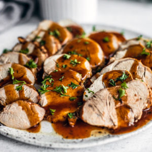 Side shot close up of platter of sliced pork tenderloin drizzled with gravy and garnished with parsley.