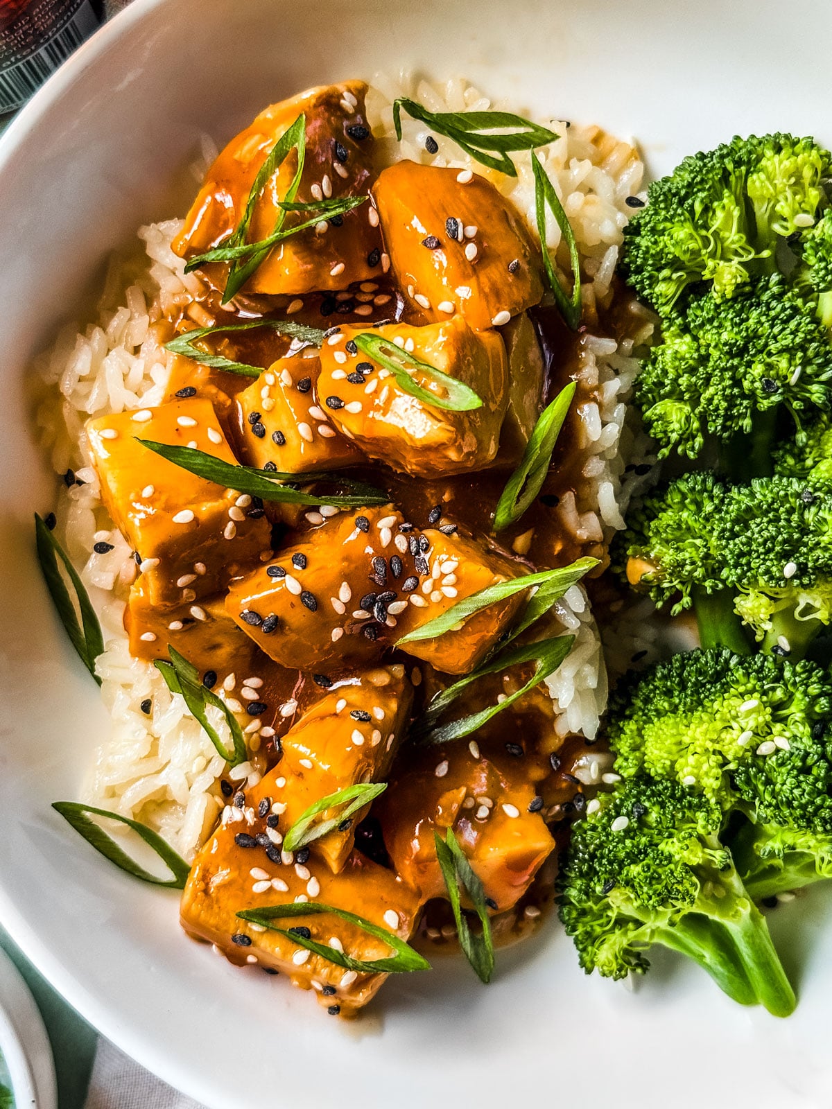 Close up of slow cooker orange chicken in a bowl with steamed broccoli.