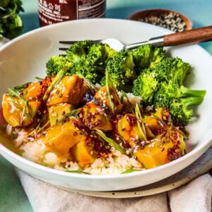 Bowl of saucy slow cooker orange chicken with steamed broccoli.