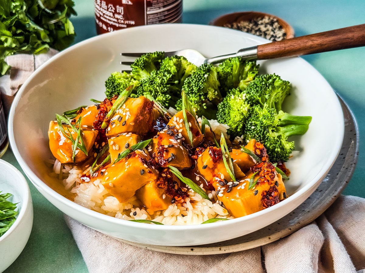 Side shot of slow cooker orange chicken in a bowl with steamed broccoli.
