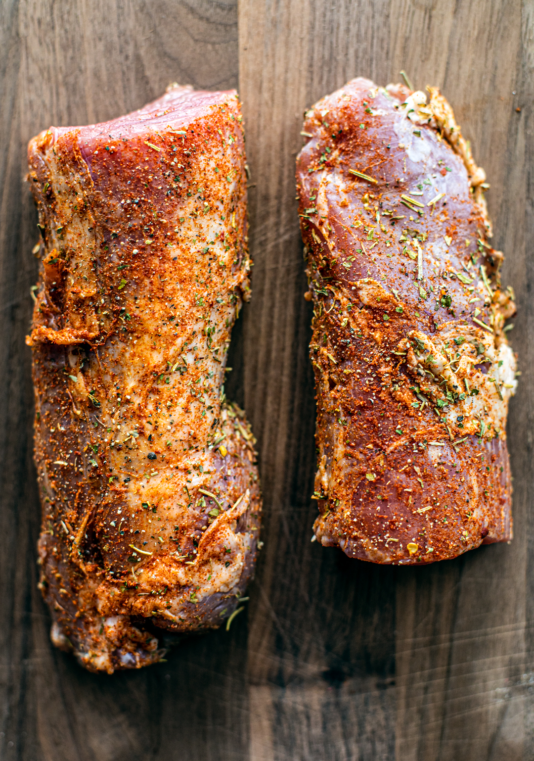 Overhead shot of raw seasoned pork tenderloin on a wooden cutting board.
