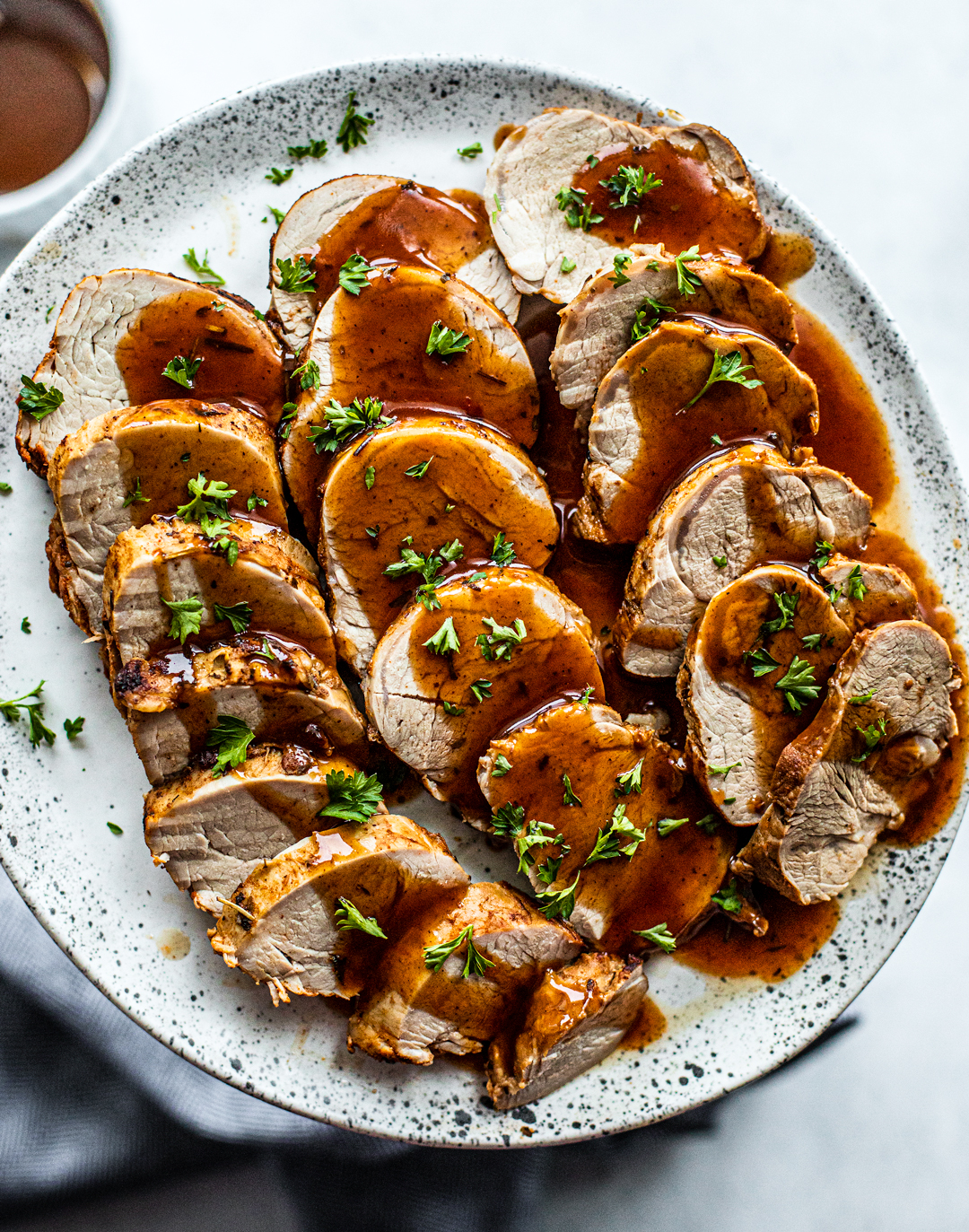 Serving platter of sliced pork tenderloin drizzled with gravy.