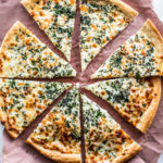 Overhead shot of cooked herb and garlic cheese pizza cut into slices on parchment paper.