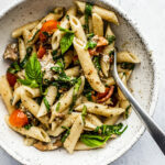 Overhead shot of a bowl of pesto pasta with tomatoes and fresh herbs.
