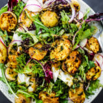 Overhead shot of a plate of roasted potatoes on greens with veggies.