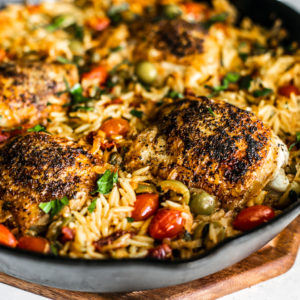 Close up side shot of crispy chicken in skillet full or orzo.
