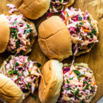 Wooden serving platter with fish sliders topped with slaw.