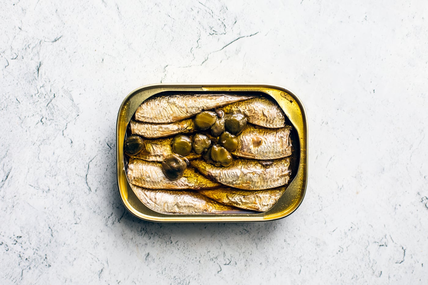 Opened can of sardines with capers on top.