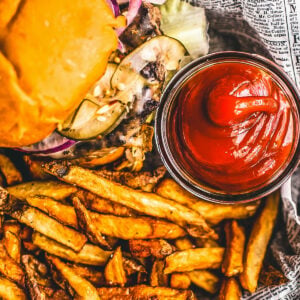 Homemade ketchup in a small glass jar next to a burger and some fries.