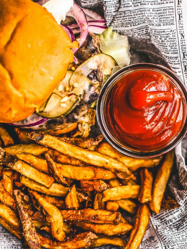 Homemade ketchup in a small glass jar next to a burger and some fries.