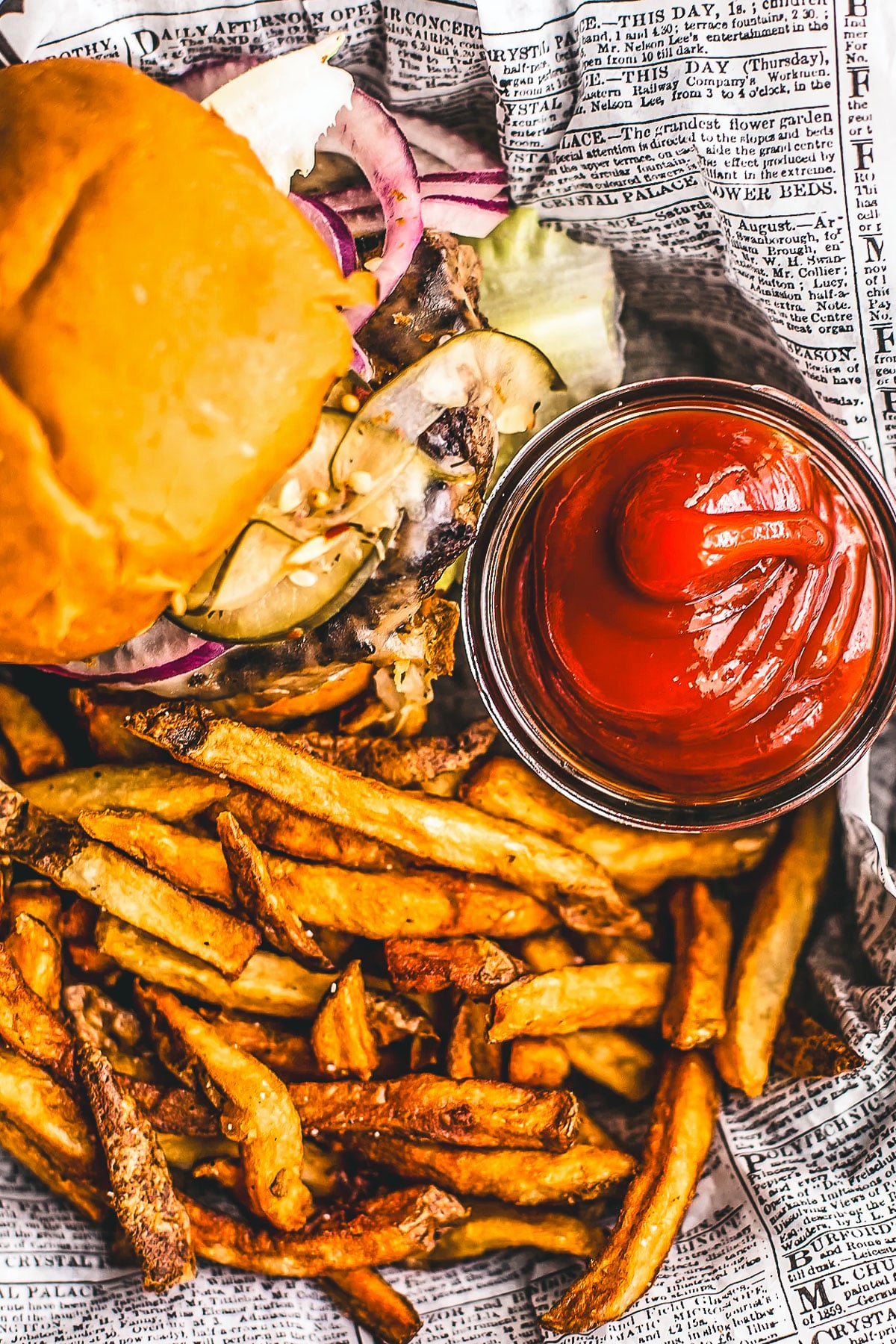 Homemade ketchup in a small glass jar next to a burger and some fries.