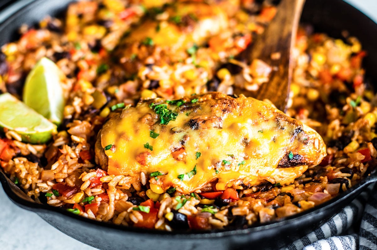Close up of cheesy chicken in skillet with rice and veggies.