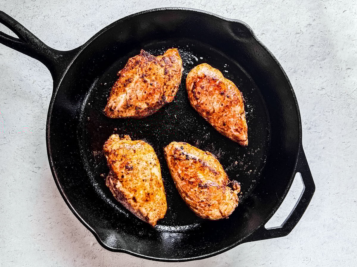 Seared seasoned chicken breasts in a cast-iron skillet.