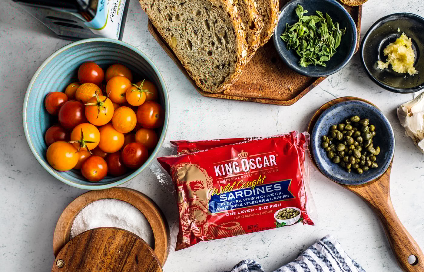 Sliced bread, bowl of cherry tomatoes, package of sardines, capers, thyme, and garlic.