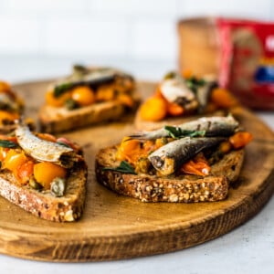 Close up of tomato confit on toast with sardines, laid out on wooden serving board.