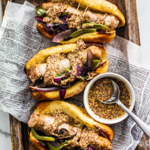 Three buns stuffed with sausage and peppers on a tray with a small bowl of mustard