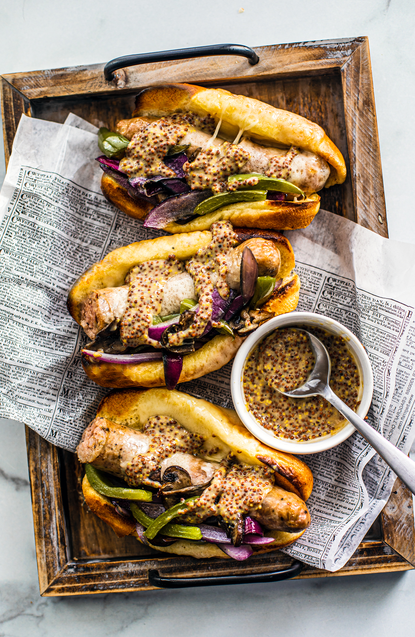 Three buns stuffed with sausage and peppers on a tray with a small bowl of mustard