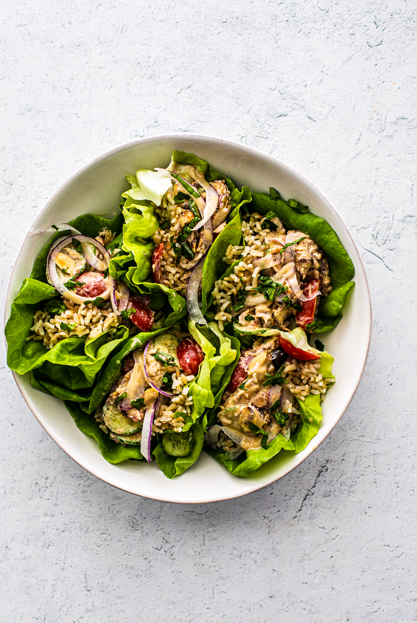 Lettuce wraps stuffed with rice and mackerel propped into a white serving bowl.