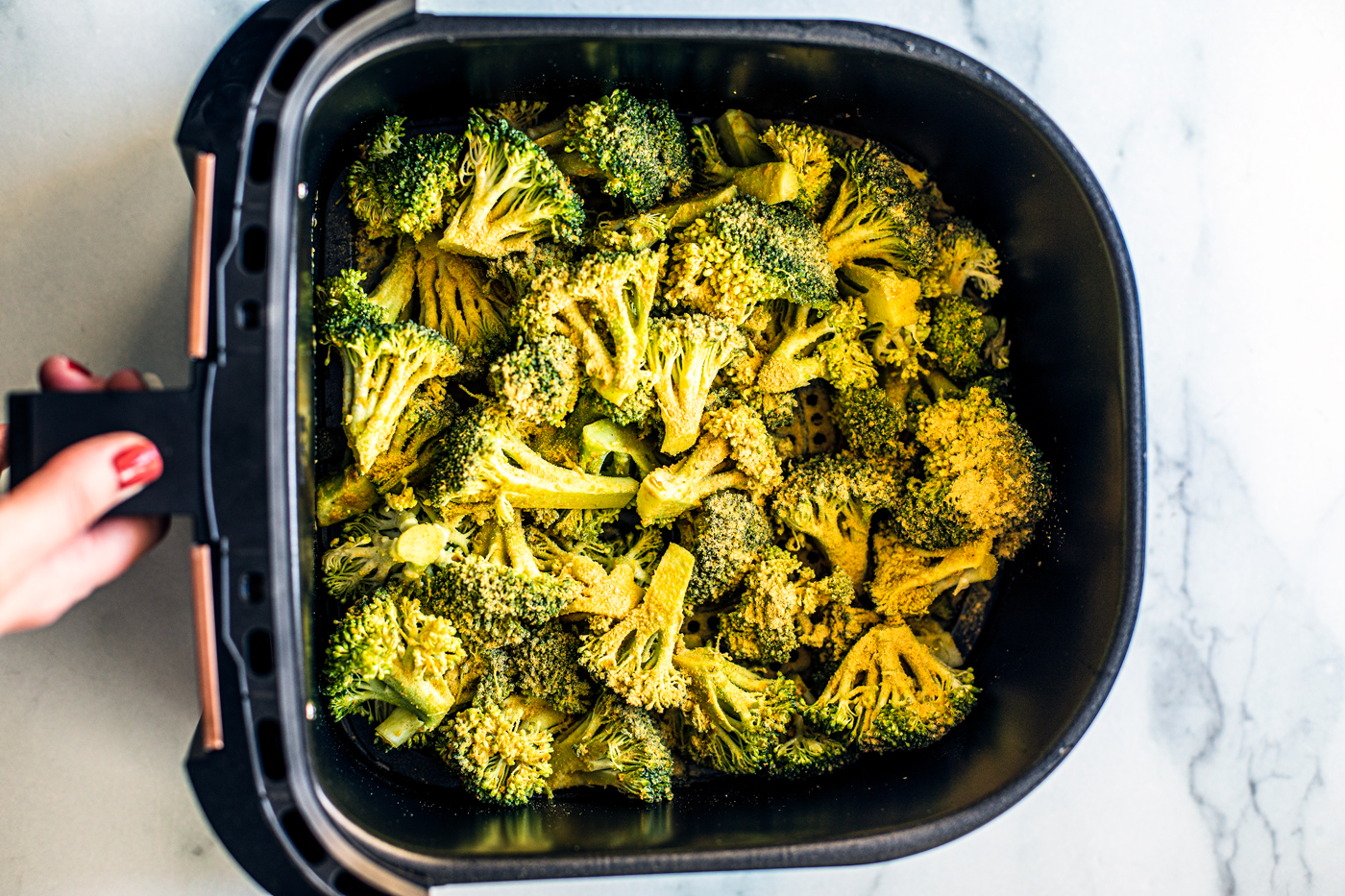 Air fryer basket with seasoned broccoli florets.