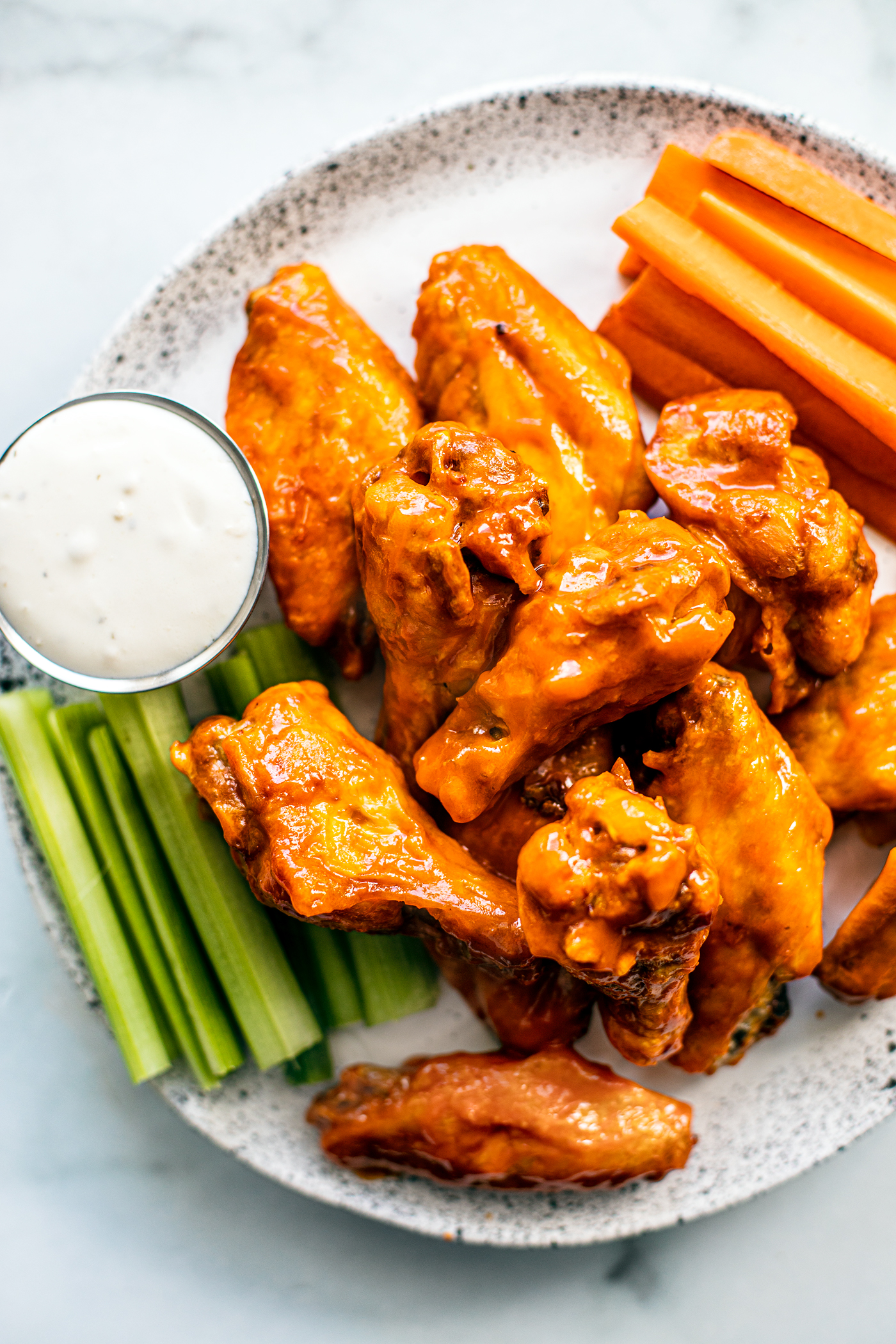  Serving plate of saucy buffalo wings with carrot and celery sticks, and blue cheese dip.