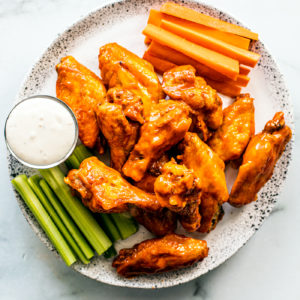 Serving plate of saucy buffalo wings with carrot and celery sticks, and blue cheese dip.