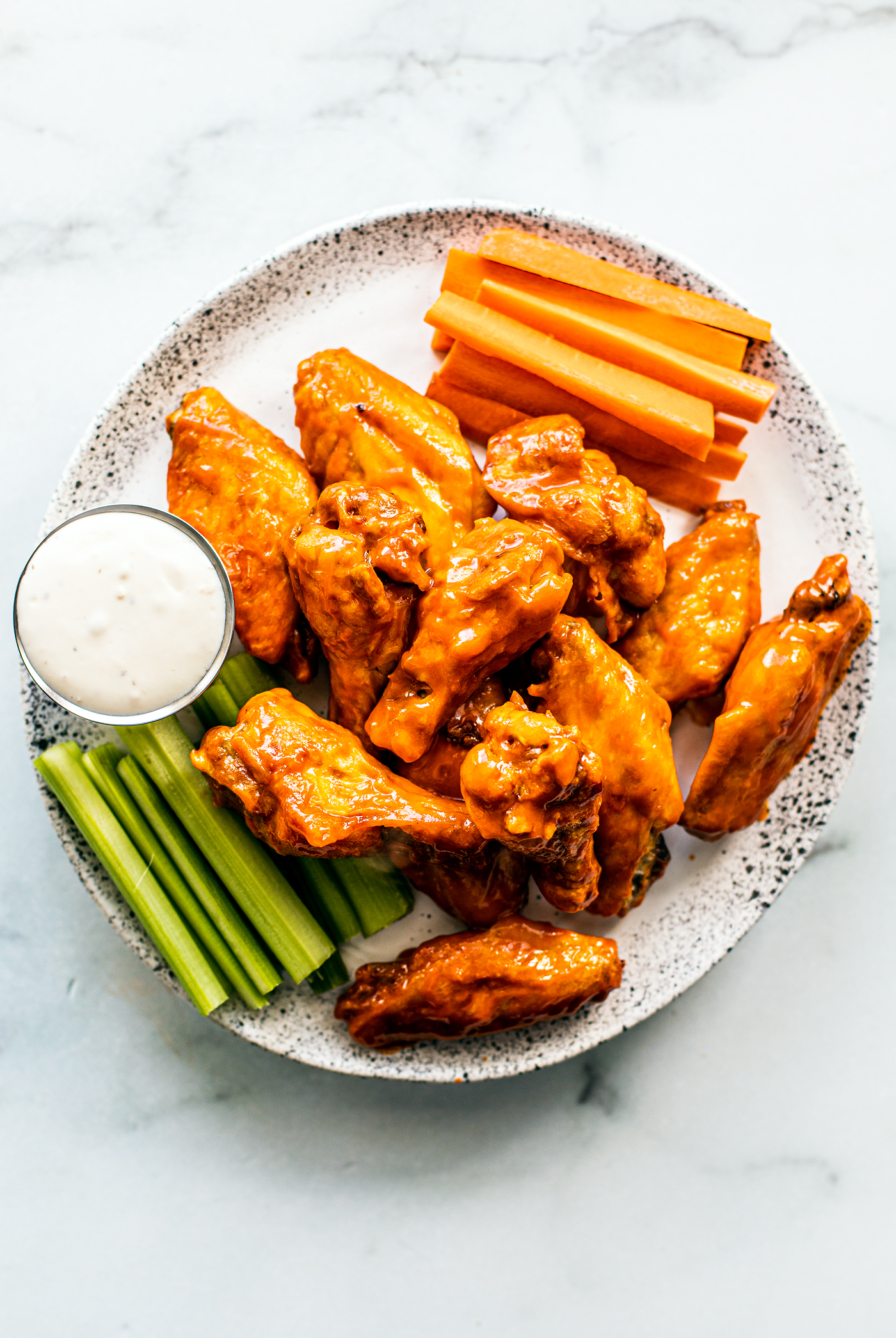 Serving plate of saucy wings with carrot and celery sticks, and blue cheese dip.