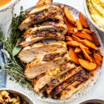 Sliced turkey breast on a serving platter with cooked carrots and fresh herbs.