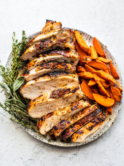 Sliced turkey breast on a serving platter with cooked carrots and fresh herbs.